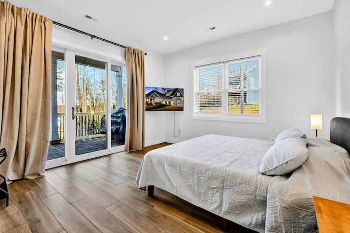 Dormitorio principal en la planta baja: puertas corredizas de vidrio que se abren al patio cubierto, con un televisor instalado en la pared y cortinas doradas que enmarcan la vista.