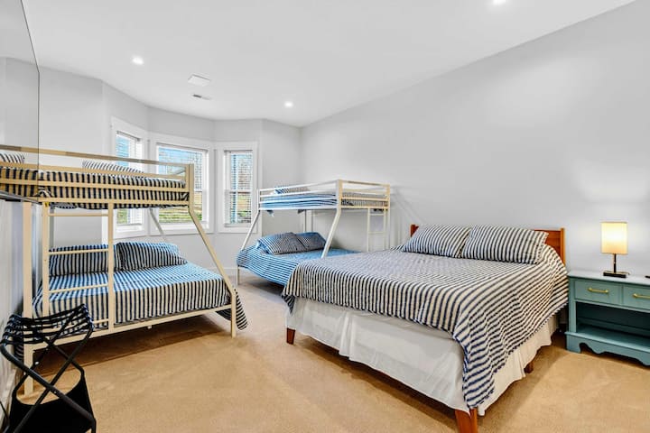 Habitación con literas: esta habitación en el nivel inferior ofrece muchas opciones para dormir, con ropa de cama a rayas en una cama queen y dos literas con una cama individual sobre una cama de una plaza.