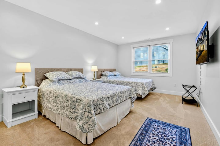 Dormitorio 6 en la planta baja: dos camas queen con ropa de cama floral a juego, un televisor de pared y una alfombra decorativa pequeña.