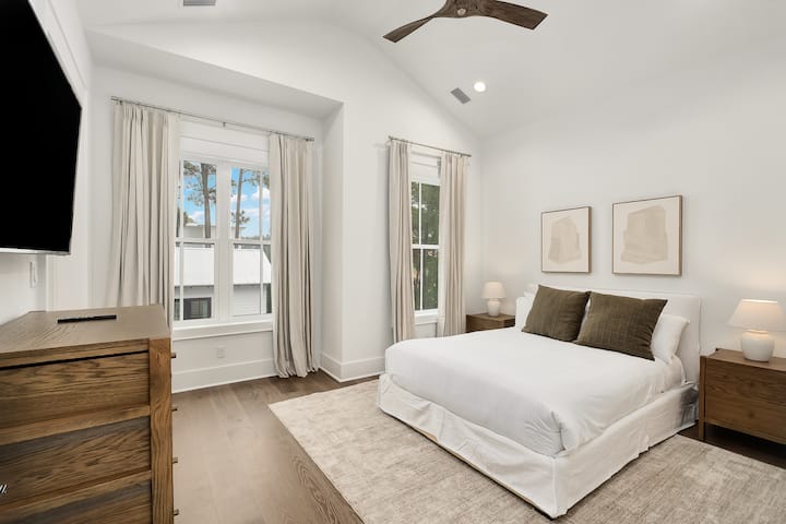 우아한 창문을 통해 자연광이 흘러들어오고 현대적인 편안함이 기다리는 침실에서 산뜻한 흰색 침구에 몸을 누이세요.