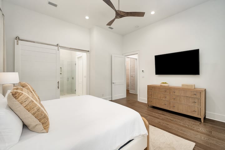 산뜻한 화이트 리넨, 따뜻한 나무 악센트, 벽걸이 TV가 있는 밝고 현대적인 침실에서 아늑한 밤을 보내세요.