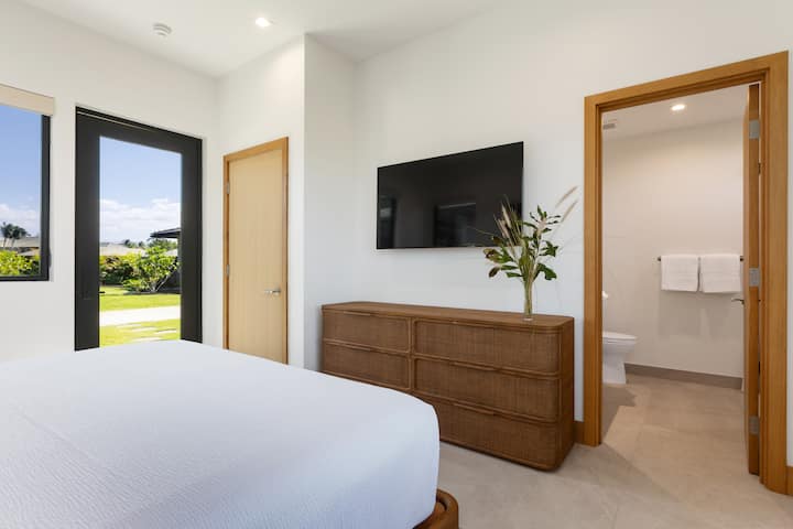 (Dormitorio 4) Tu dormitorio sereno cuenta con sábanas blancas nítidas, un televisor montado en la pared para relajarse y vistas al jardín a través de grandes ventanales.