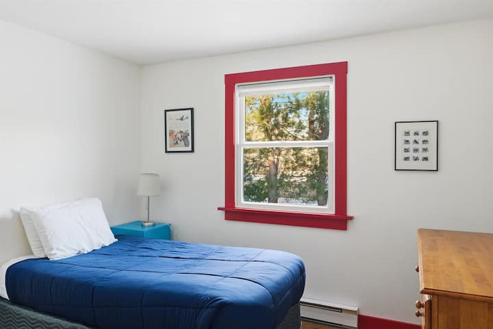 ห้องนอนส่วนหน้าที่สว่างไสวมีเตียงแฝดที่สะดวกสบายและวิวของสนาม ห้องที่เงียบสงบนี้เหมาะสำหรับเด็กหรือนักเดินป่าเดี่ยว มอบการพักผ่อนที่เงียบสงบภายในปีกหลักที่ใช้สำหรับนอนของคอทเทจ