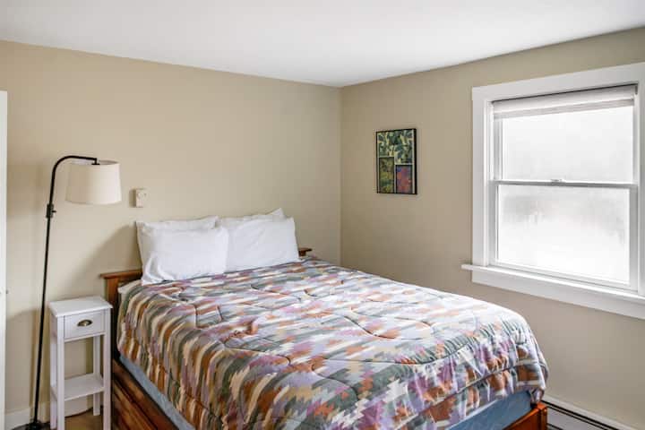 วิวเต็มรูปแบบของห้องนอนหลักที่มีเตียงควีนไซส์ในปีกด้านหน้า ที่พักที่สว่างสดใสแห่งนี้มีโต๊ะข้างเตียงพร้อมโคมไฟอ่านหนังสือ และมีพื้นที่กว้างขวางให้คุณได้พักผ่อนอย่างเต็มที่หลังจากออกสำรวจเส้นทางเดินป่าในออตเตอร์ครีก