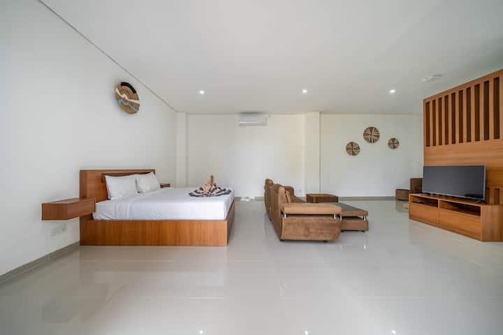 Quarto iluminado com cama king, sofá e TV