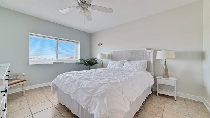 Habitación de invitados luminosa y espaciosa con cama tamaño queen, una paleta blanca clásica y muebles elegantes, creando un ambiente relajante.