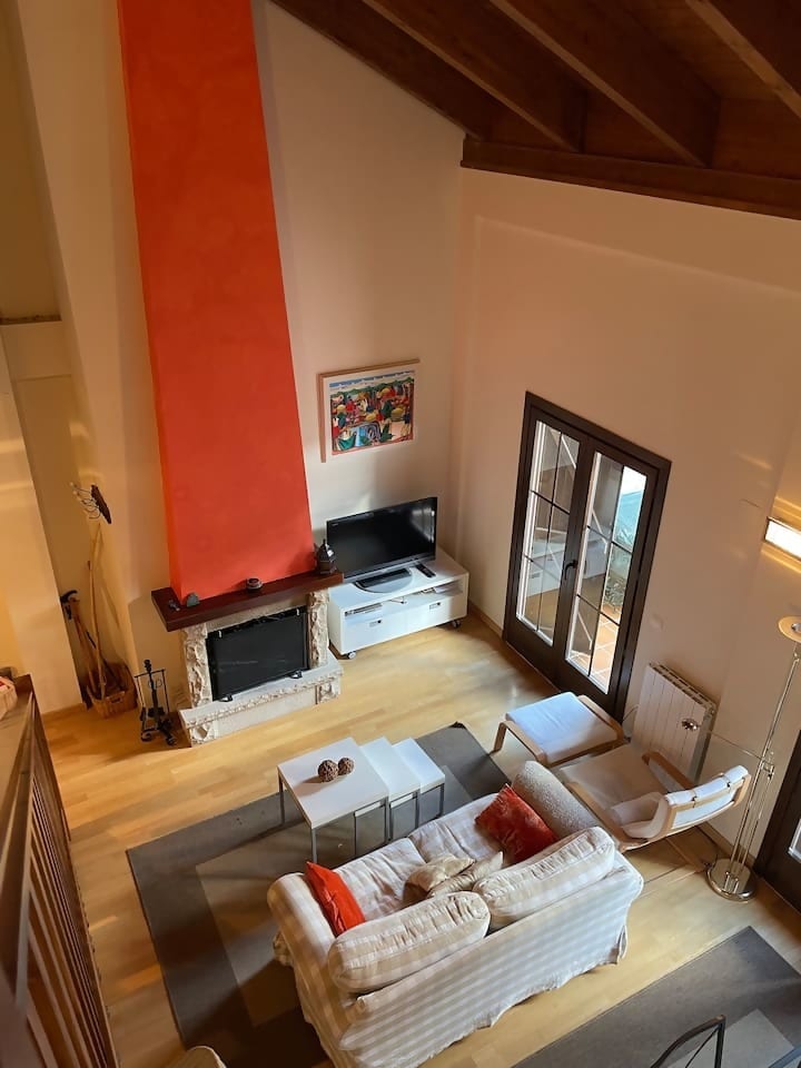 An overview of the spacious living area highlights a comfortable sofa adorned with orange cushions and a coffee table. A Smart TV is positioned on a white console, while a red accent wall adds warmth. Natural light streams through double doors leading to the terrace.