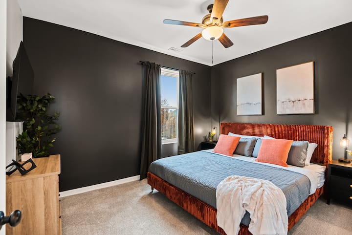 Elegante dormitorio moderno: cuenta con una lujosa cama tamaño queen con una cabecera de terciopelo llamativa, televisor inteligente montado en la pared e iluminación industrial elegante para una sensación de alta gama.