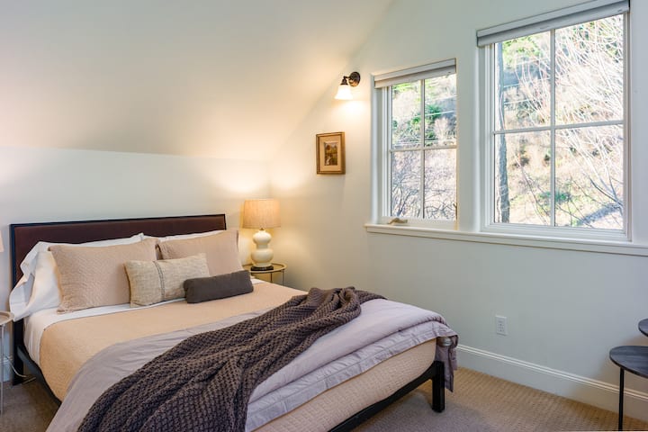 חדר שינה נעים ומלא אור עם מצעים קטיפה ונופים שלוים של צמרות עצים ללילות שלוים.