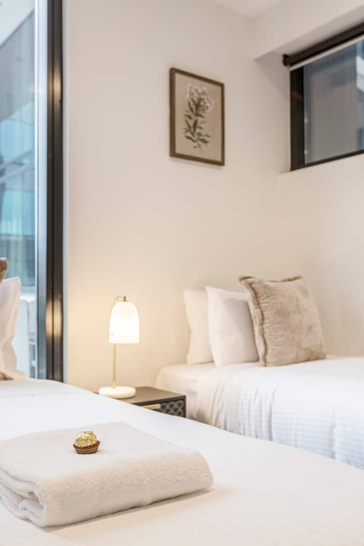 Habitación doble luminosa con sábanas de lujo, vistas a la ciudad y detalles de bienvenida