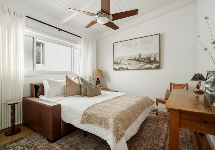 Un bureau-chambre polyvalent avec un canapé-lit Queen Size confortable, des textures naturelles chaleureuses et un bureau dédié, idéal pour le travail à distance le jour et un sommeil réparateur la nuit.