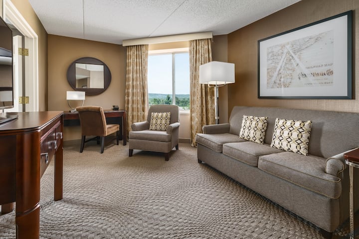 Obývacia izba v apartmáne s pohovkou, kreslom a pracovným stolom pri okne