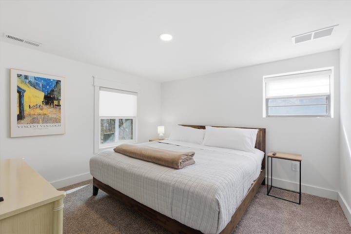 Súkromná spálňa s manželskou posteľou na nižšom poschodí s mäkkým kobercom, teplými drevenými prvkami a pokojným prirodzeným svetlom. Pokojné útočisko ideálne pre hostí, ktorí chcú mať viac súkromia.