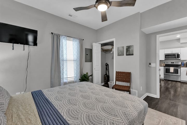 Udobna spavaća soba s bračnim krevetom, TV-om, stropnim ventilatorom i stepenicama koje vode do moderne kuhinje C