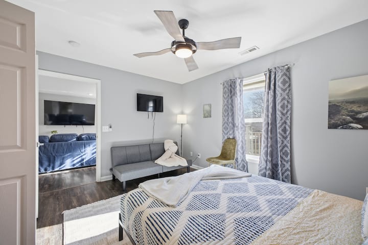 Svijetla spavaća soba s bračnim krevetom, futonom, pametnim televizorom i prozorom s pogledom na vjetrovitu jedinicu E