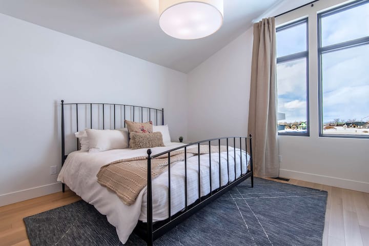 Guest bedroom with iron bed frame, crisp white linens, and a Teton-view window — understated elegance that still packs a serious visual punch.
