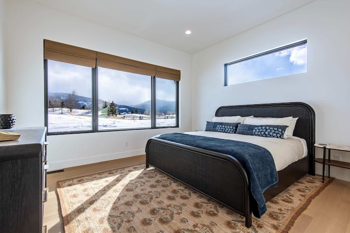 Primary bedroom with king bed, navy accent bedding, and sweeping Teton views through the window — fall asleep with the mountains in full view.