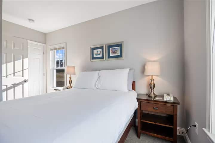 Dormitorio luminoso y acogedor con cama tamaño queen, dos lámparas y ventanas soleadas
