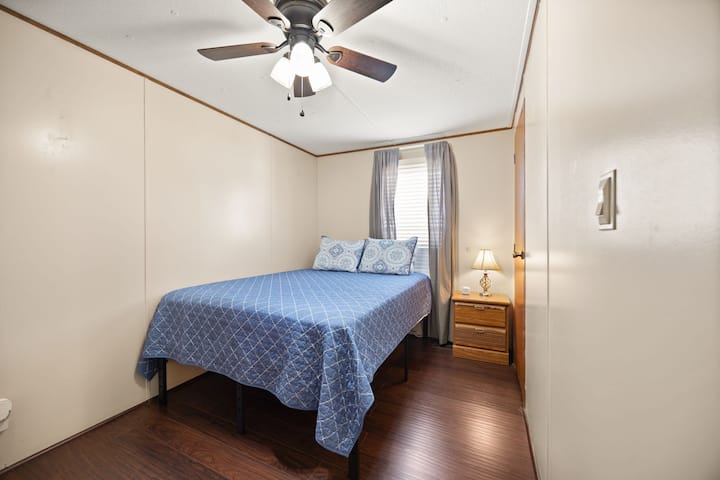Dormitorio luminoso y acogedor con cama completa, ventilador de techo y pisos de madera noble