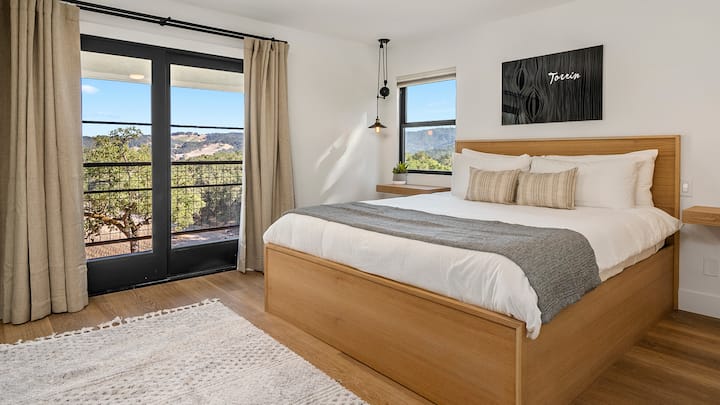 Sleep in comfort on a plush king-size bed while enjoying bright natural light and scenic hillside views.