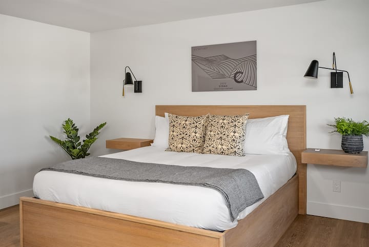 A minimalist bedroom with a wooden California King bed, floating nightstands, and an ultra-puffy mattress.