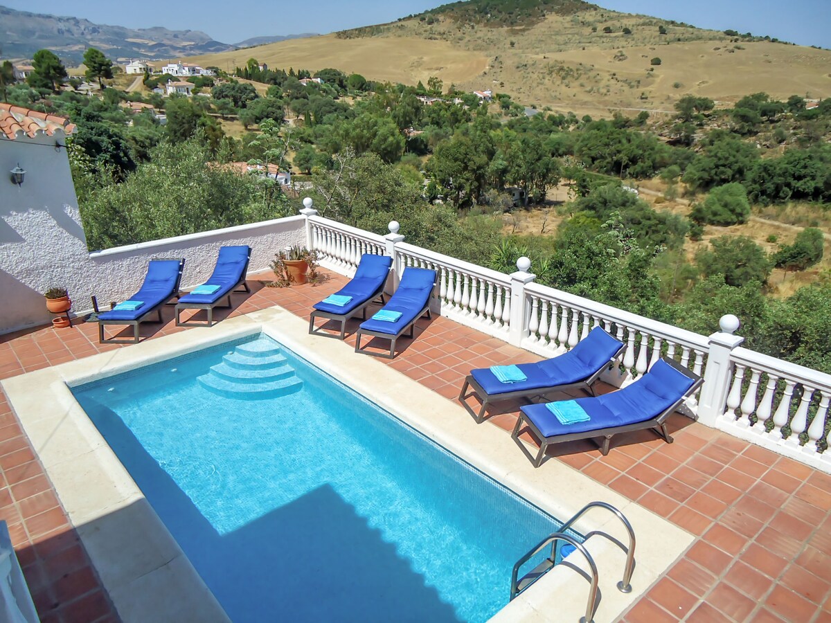 A private swimming pool is situated on a terrace, surrounded by six blue lounge chairs. A view of rolling hills and greenery is visible in the background, creating a serene outdoor space for relaxation.