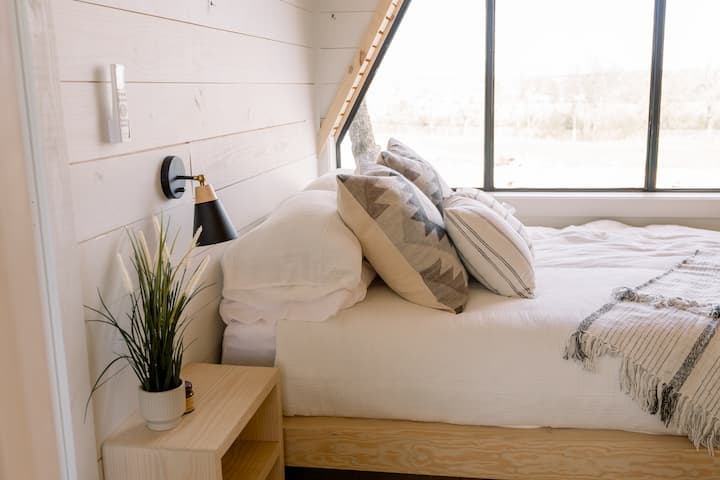 Sunny, minimalist loft bedroom with cozy bedding and big picture window views
