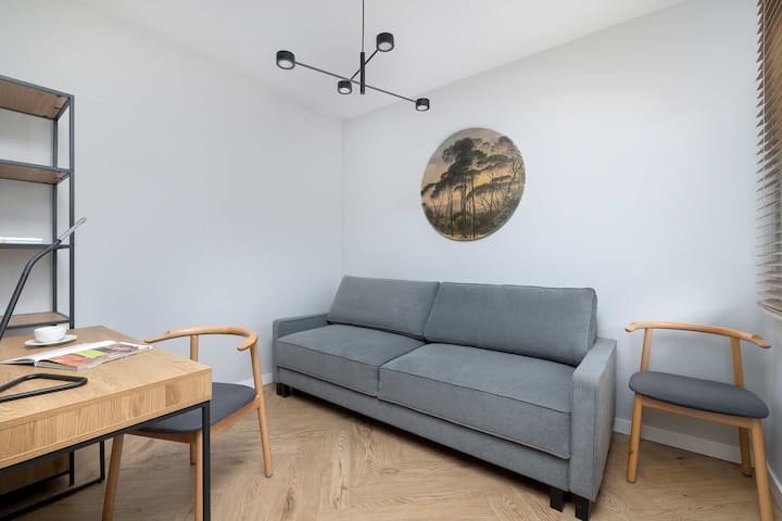 Una habitación minimalista para huéspedes cuenta con un sofá gris y un sencillo escritorio de madera con una silla. Un mapamundi circular en la pared sirve como un sutil elemento decorativo.