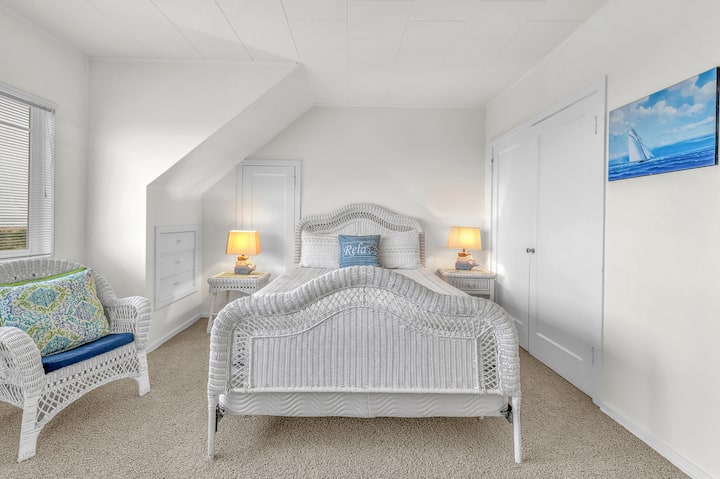 Tu refugio costero con dormitorio te espera con muebles de mimbre blanco, iluminación suave y detalles náuticos que prometen noches tranquilas junto al mar.