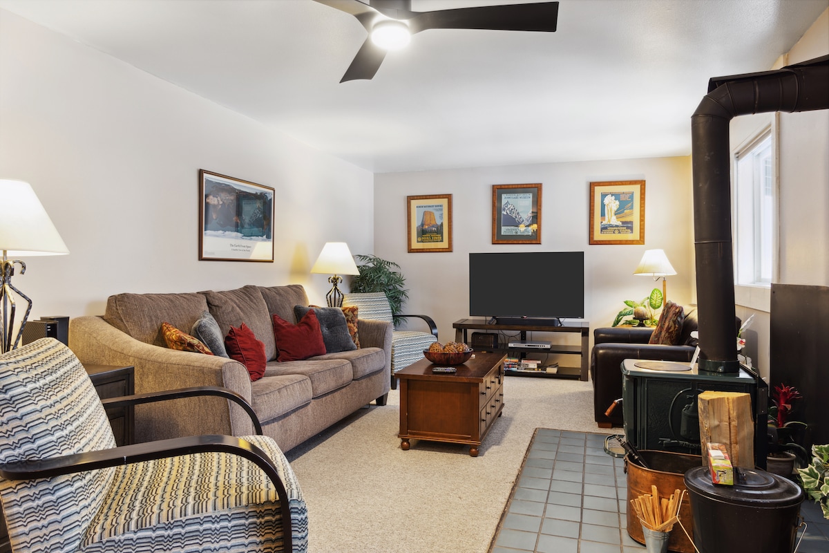 The living area features a spacious couch adorned with pillows, complemented by a loveseat and an armchair. A coffee table occupies the center, and a flat-screen TV is mounted on the wall. A woodburning stove stands in the corner, providing warmth and comfort.