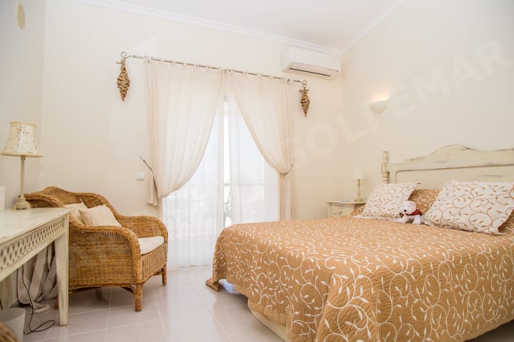 Dhomë gjumi joshëse në apartamentin Vila Golfemar me një krevat dopio të rehatshëm me kokë krevati prej xunkthi, perde të bardha që valëviten dhe dekor të ngrohtë në stil mesdhetar për një pushim të rehatshëm në Algarve