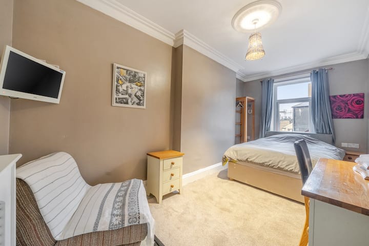 Chambre avec un lit, un coin bureau et une télévision fixée au mur.