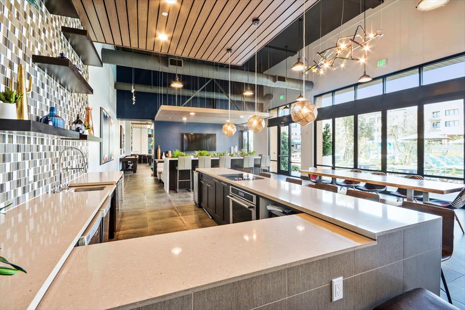 The community kitchen showcases modern design elements with sleek countertops and pendant lighting. A tiled backsplash adds a stylish touch, while large windows provide ample natural light. The layout includes spacious seating and dining areas, creating an inviting atmosphere for social gatherings.