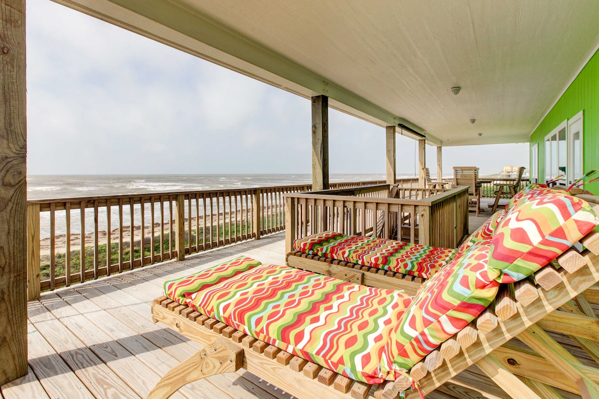 An ocean-facing deck provides a spacious area with several lounge chairs featuring vibrant cushions. The deck is surrounded by wooden railings and offers views of the Gulf waves, enhancing the outdoor living experience.