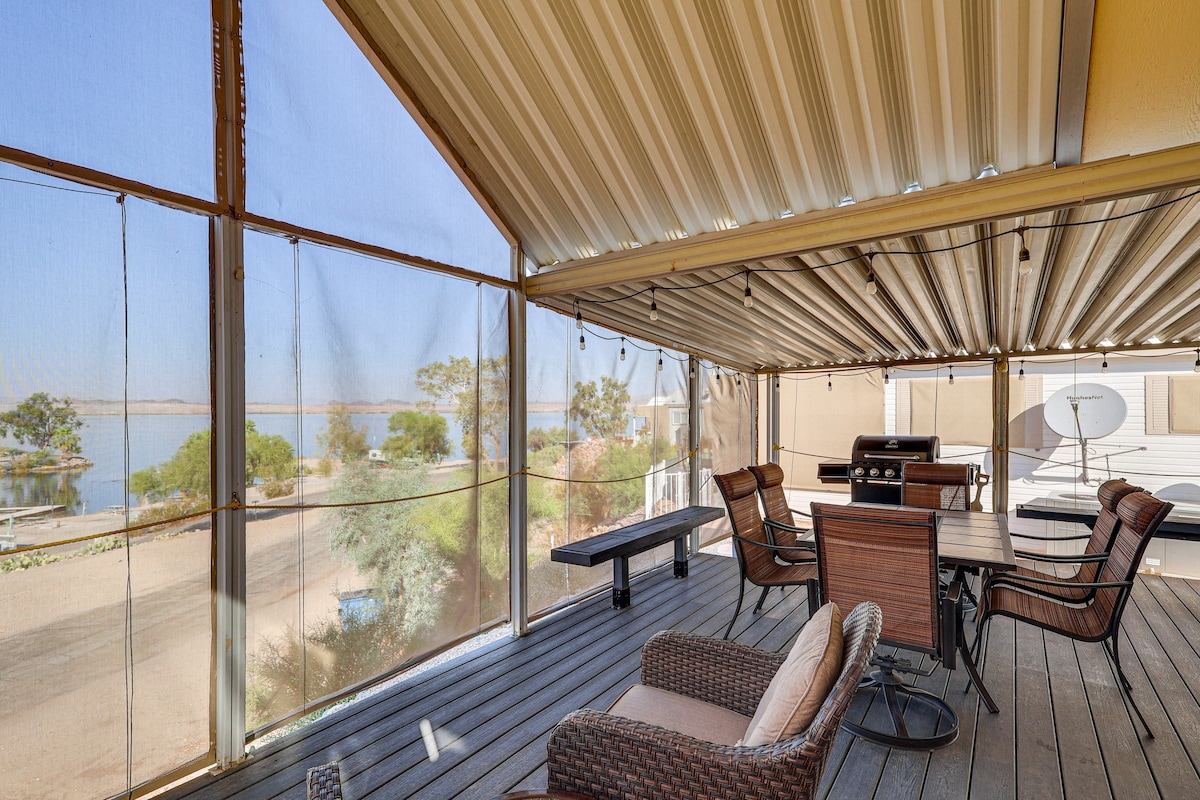 A screened-in deck offers views of the water, furnished with a dining table and several lounge chairs. The space is illuminated by soft lighting, providing a relaxed atmosphere for outdoor gatherings. A gas grill is positioned nearby for easy outdoor cooking.