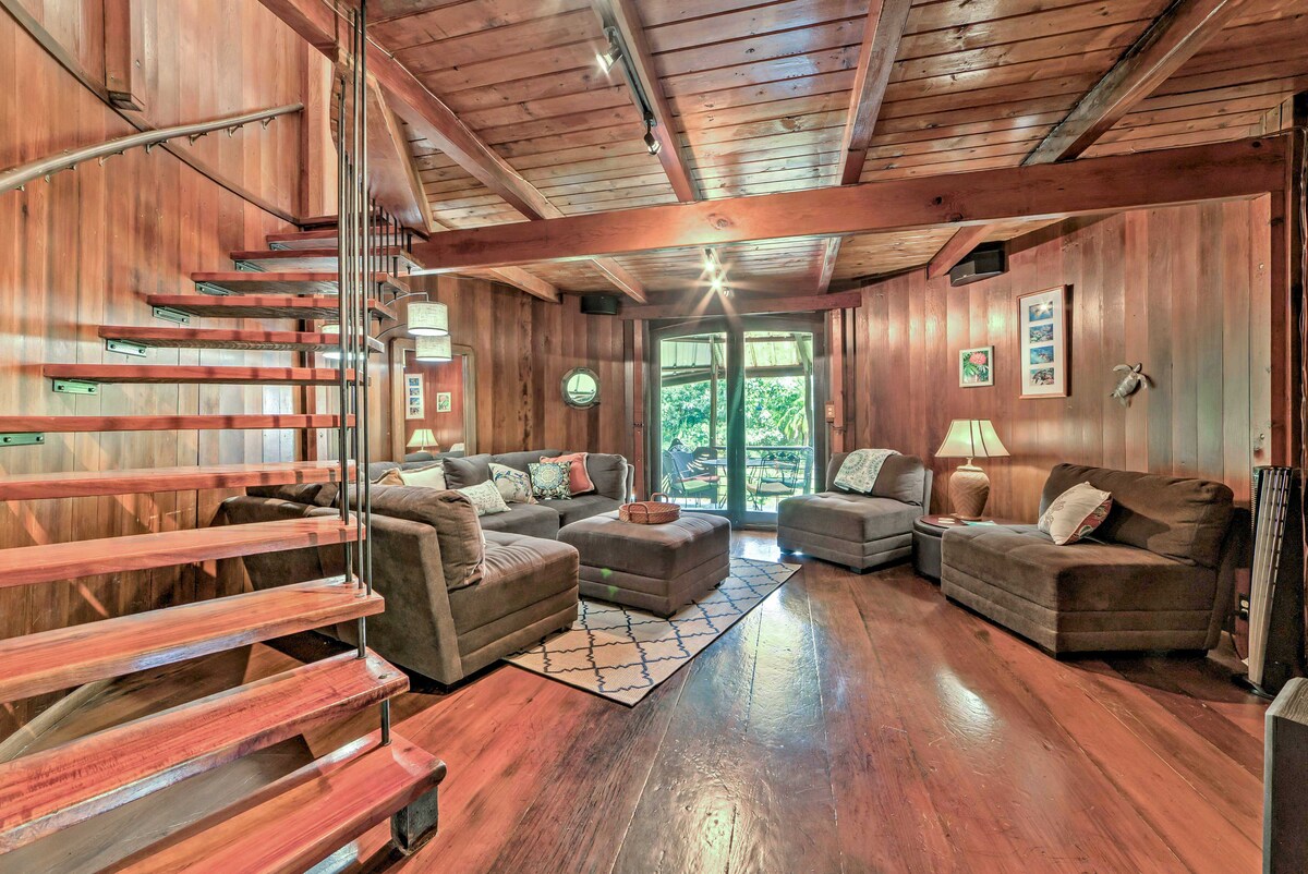 A spacious living area features warm wooden paneling and exposed beams, creating a cozy atmosphere. A sectional sofa surrounds a central coffee table, while large sliding doors provide access to the outdoor deck, inviting natural light into the space.