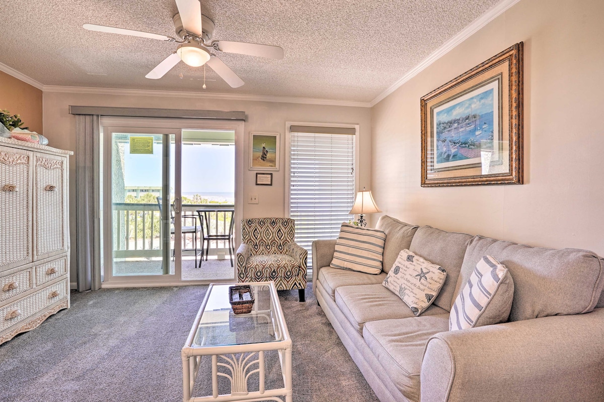The living area features a light-colored sofa accompanied by a patterned armchair, creating a comfortable seating arrangement. A glass coffee table sits in the center, while sliding glass doors lead to the balcony, allowing natural light to fill the space.