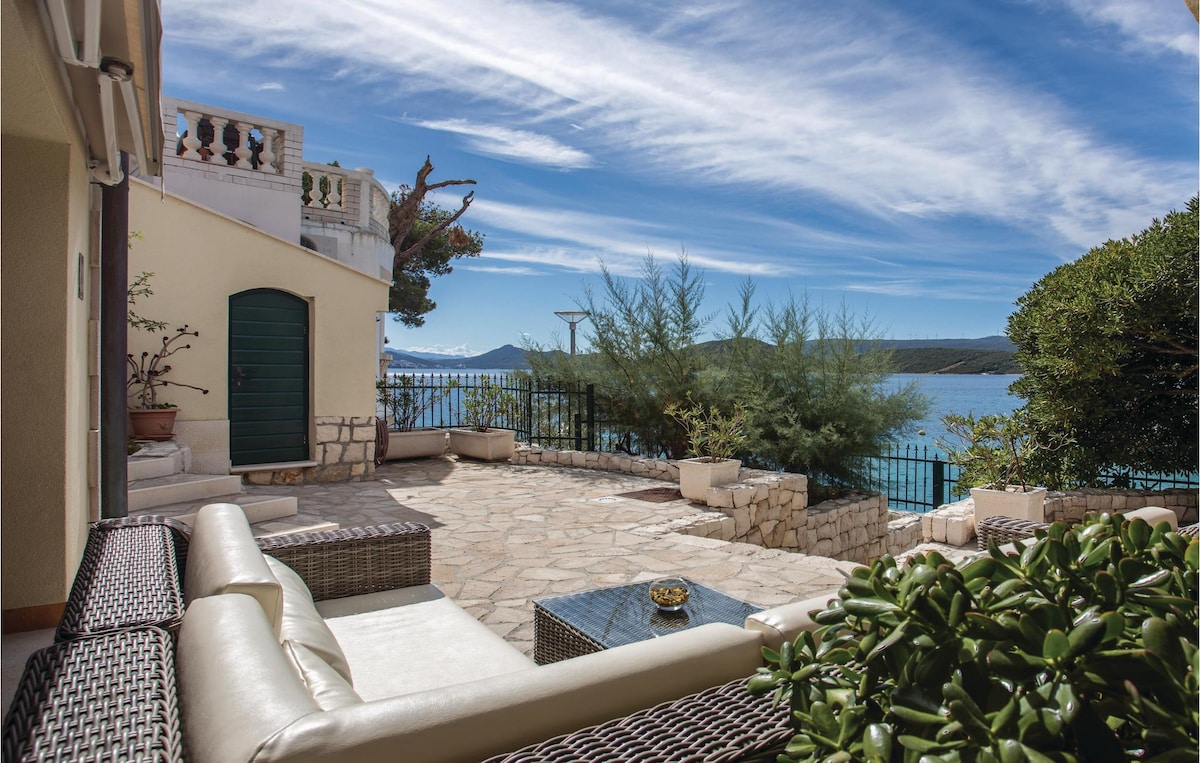 A spacious terrace offers a relaxing seating area with comfortable furniture, framed by lush greenery. The tranquil sea view is complemented by a clear blue sky, enhancing the outdoor atmosphere. Decorative planters add a touch of nature to the setting.