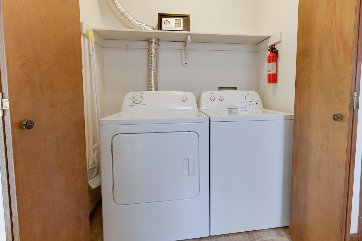 A laundry area is shown featuring a stacked washer and dryer, positioned side by side on a tiled floor. Additional storage space is provided above the appliances, and a fire extinguisher is mounted on the wall for safety.
