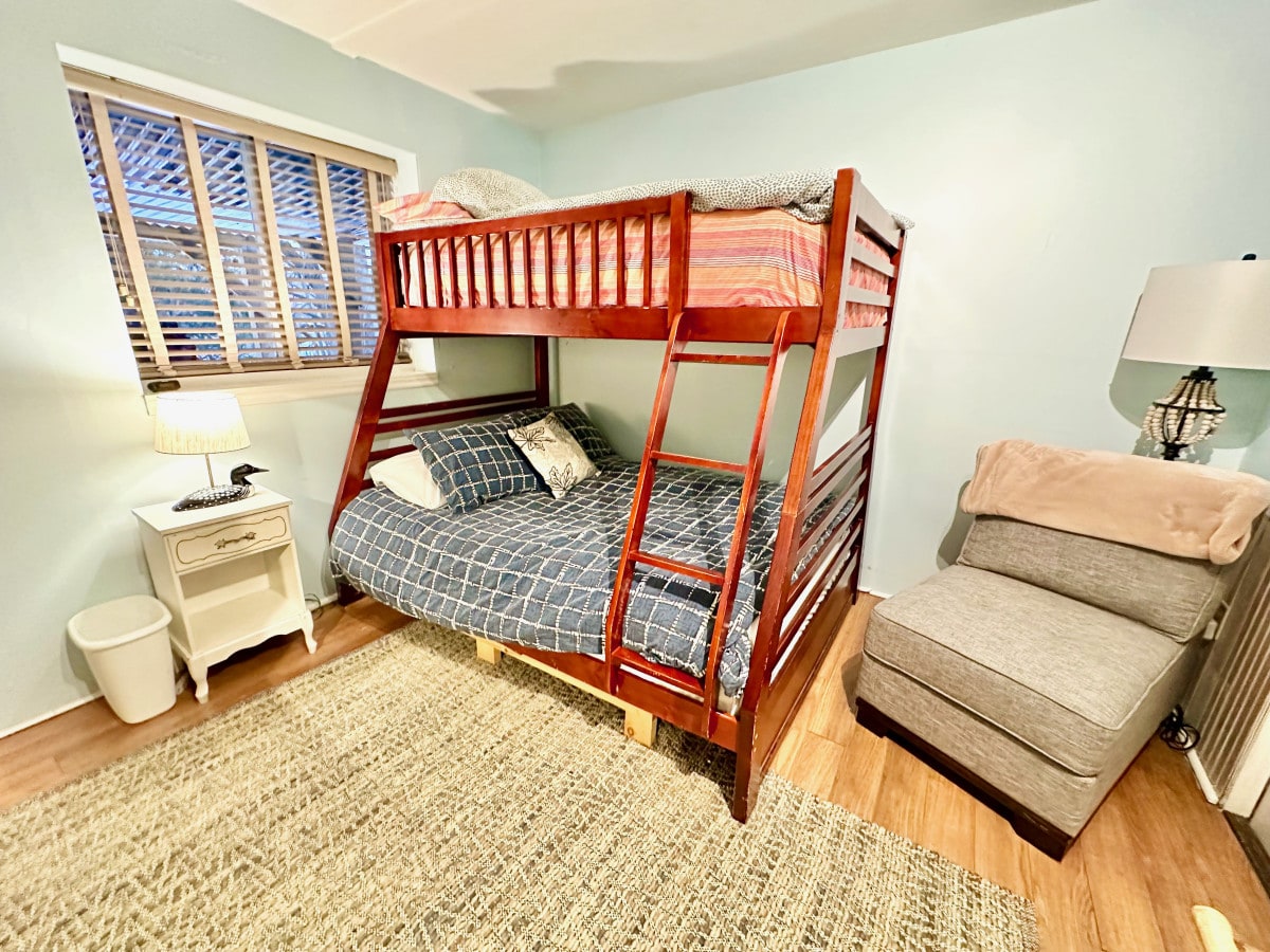 Spavaća soba br. 4 u prizemlju, opremljena krevetima na kat s bračnim krevetom, krevetom za jednu osobu i stolicom. Ima prozor s pogledom na rijeku.