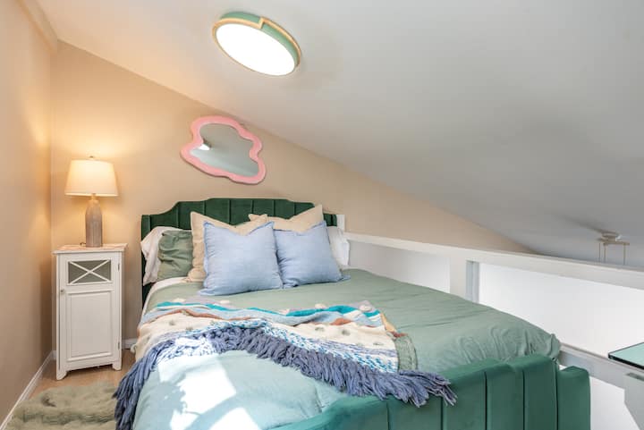 Útulná manželská posteľ s televízorom v otvorenom hornom lofte vedľa dvojlôžka