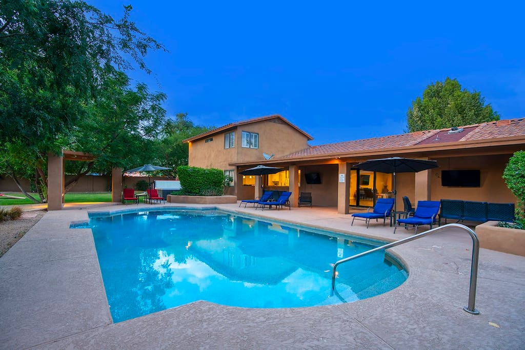 A private pool area is featured, surrounded by lush greenery and lounge chairs. An inviting pool is complemented by an outdoor seating arrangement under a shaded umbrella. The property highlights a rustic design, seamlessly blending with the tranquil environment.