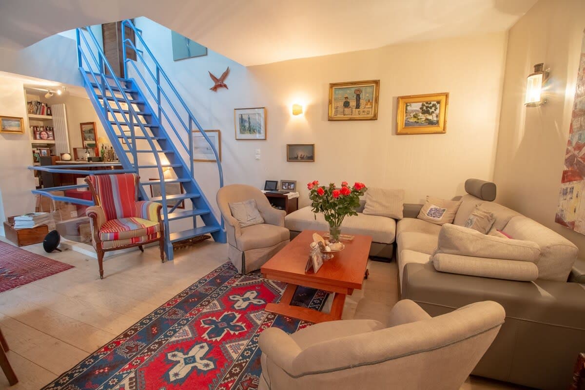 A welcoming living area features a light color palette with comfortable seating arranged around a wooden coffee table. A bouquet of flowers rests on the table. Unique artwork adorns the walls, and natural light enters through a nearby window, highlighting the cozy atmosphere.