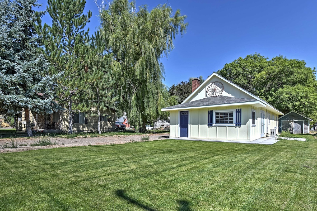 A charming cottage is showcased within a spacious yard, surrounded by lush greenery. Mature trees provide shade, while a vibrant blue sky enhances the inviting exterior of the home. A well-maintained lawn complements the neat design of the property.