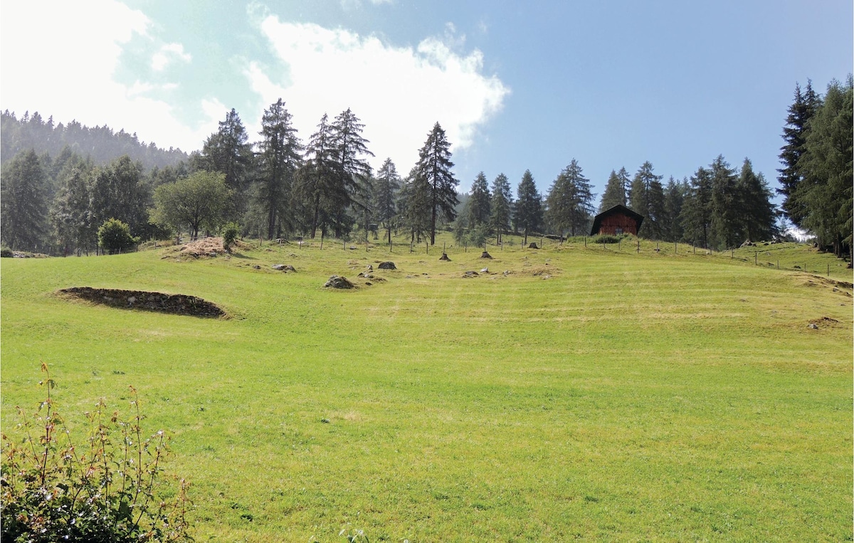 A vast green landscape is depicted, featuring a gentle slope that leads to a rustic wooden cabin. Tall trees are scattered throughout, and a clear blue sky is visible, with a few fluffy clouds adding texture to the scene.