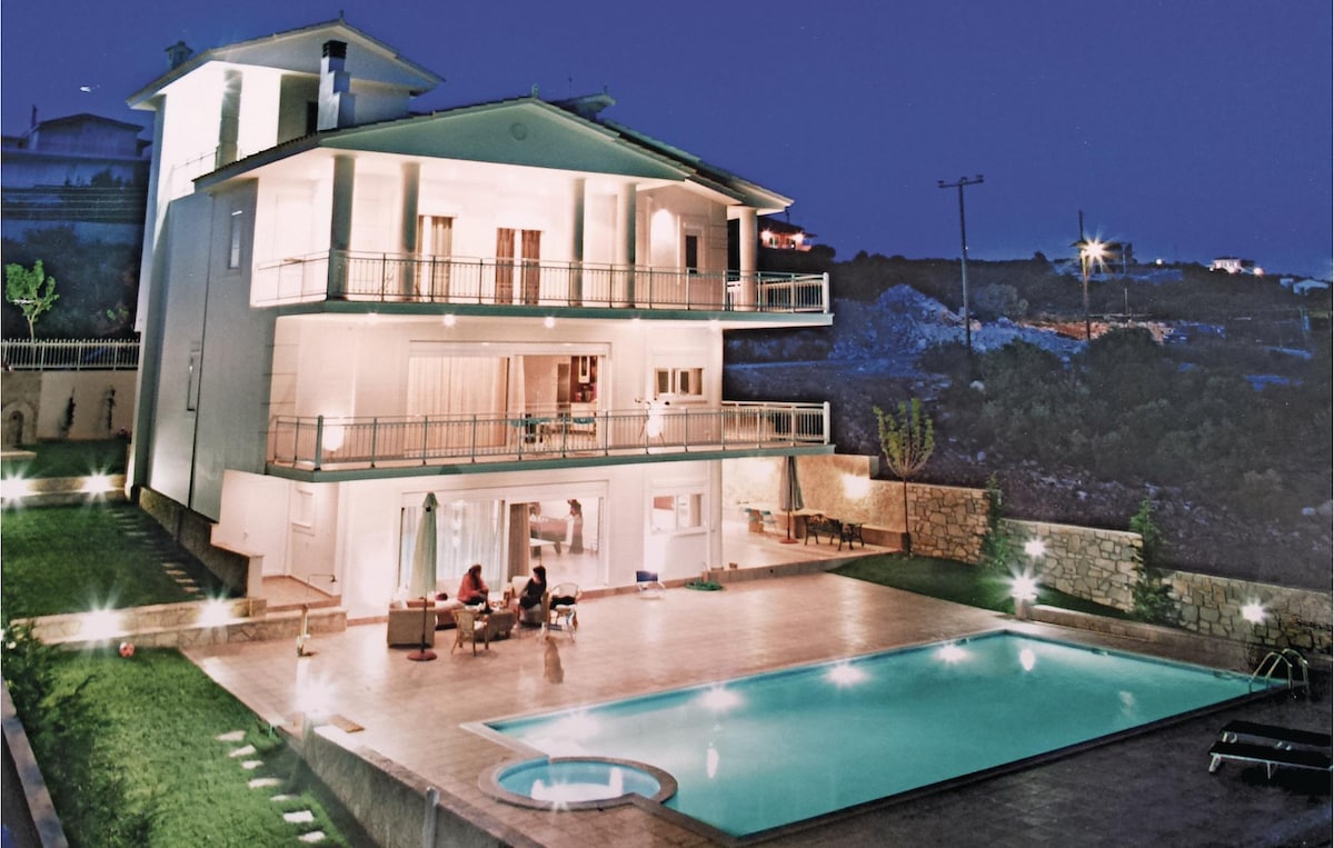 The villa is illuminated at night, revealing three spacious levels and a large swimming pool surrounded by a tiled patio. Overhead, soft lighting highlights the structure’s modern design. The outdoor area is complemented by well-maintained green spaces, creating an inviting atmosphere for gatherings.