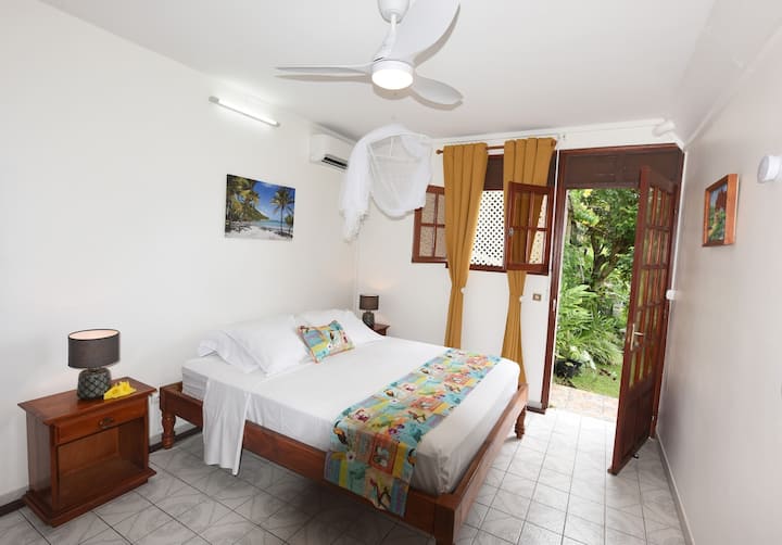Habitación principal luminosa  con cama de 160 cm x 200 cm,  que da al jardín aromático desde donde tendrá una vista panorámica del mar información sobre Fleurs de Poirier — ambiente tropical y noches tranquilas bajo mosquitero.