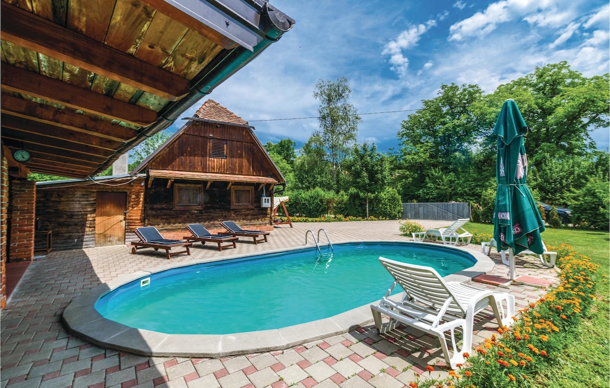 A private outdoor pool is framed by sun loungers, offering a space for relaxation. The surrounding garden features well-maintained greenery and colorful flower borders. A rustic-style house is visible in the background, accompanied by a shaded umbrella for additional comfort.