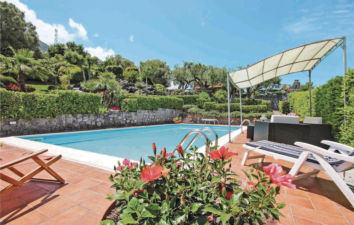 A private outdoor pool is surrounded by a spacious deck with lounge chairs. Lush green gardens and vibrant flowers frame the pool area, providing a serene setting. A shaded seating area is visible, inviting relaxation under the sun.