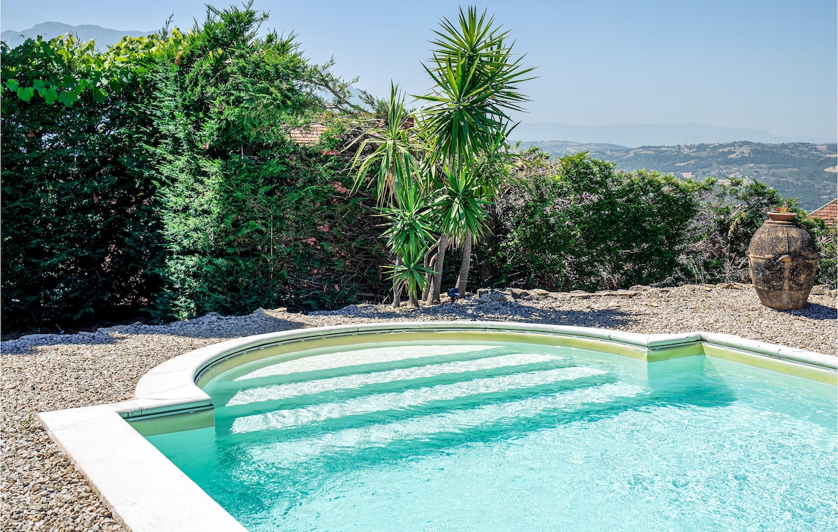 A serene outdoor space features a private swimming pool with steps leading into the water. Surrounding greenery provides privacy, and a decorative pot adds a rustic touch to the landscape. The clear water reflects the bright sky, creating a peaceful atmosphere.